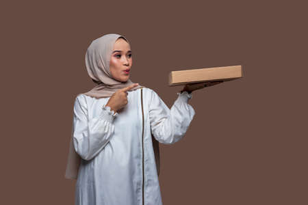 Surprise woman in hijab holding a pizza box with one left hand and her right hand pointingの写真素材