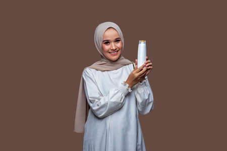 Beautiful woman in hijab was holding shampoo bottle in both hands while looking at the cameraの写真素材