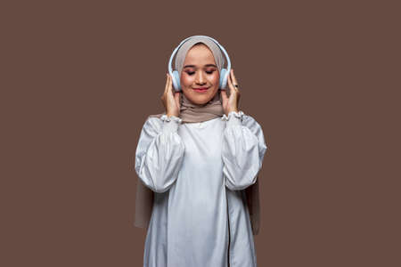 Beautiful Asian women wearing hijab using wireless headphones are enjoying listening to music while closing their eyesの写真素材