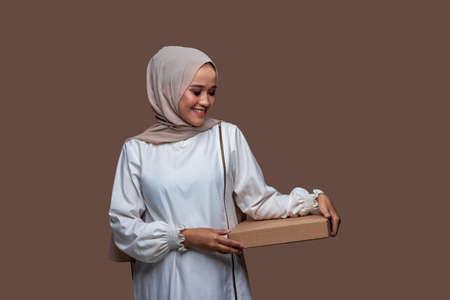 Beautiful asian woman in hijab holding pizza box with both hands while smilingの写真素材