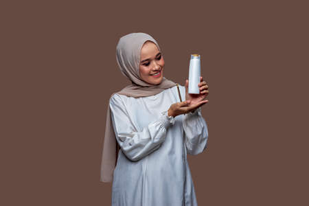 Beautiful indonesian woman in hijab was holding a shampoo bottle with her left hand and her right hand pointing at itの写真素材