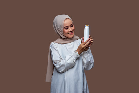 Beautiful hijab woman was holding shampoo bottle in both hands while looking at the bottleの写真素材