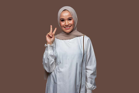 Beautiful indonesian hijab women with peaceful hand gestures isolated on plain backgroundの写真素材