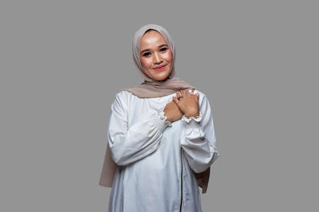 Beautiful hijab woman posing holding the chest with a smile isolated on plain backgroundの写真素材