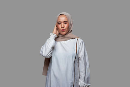 Beautiful woman wearing hijab is dizzy while touching head isolated on plain backgroundの写真素材
