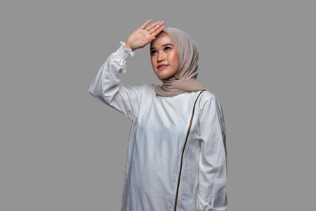 Beautiful woman is looking up and posing raises one hand while smiling isolated on plain backgroundの写真素材