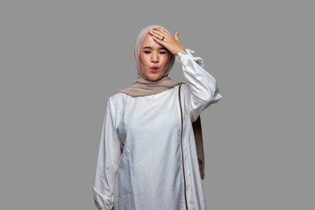 Beautiful woman wearing hijab is dizzy while touching the front of the head isolated on plain backgroundの写真素材