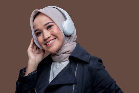 Asian hijab woman wearing wireless headphones with a smile looking at the camera.の写真素材