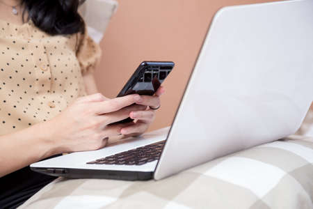 Woman sitting on chair with laptop at table holding drinking glass and looking at screenの写真素材