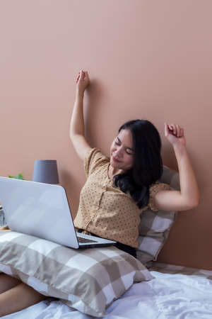 Woman sitting on chair with laptop at table holding drinking glass and looking at screenの写真素材