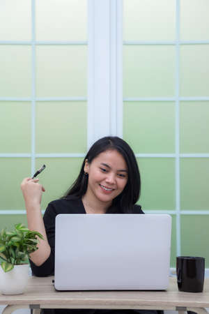 Woman sitting on chair with laptop at table holding drinking glass and looking at screenの写真素材