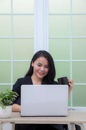 Woman sitting on chair with laptop at table holding drinking glass and looking at screenの写真素材
