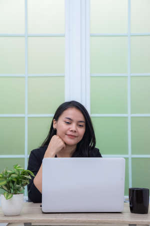 Business woman sitting on chair with laptop on table while holding drinking glass and smilingの写真素材