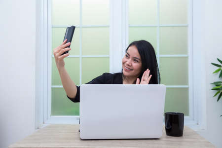 Business woman sitting on chair with laptop on table while holding drinking glass and smilingの写真素材