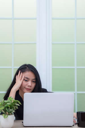 Business woman sitting on chair with laptop on table while holding drinking glass and smilingの写真素材