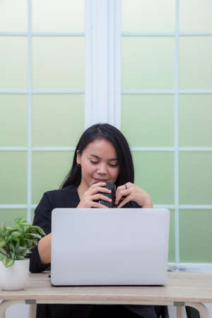 Business woman sitting on chair with laptop on table while holding drinking glass and smilingの写真素材