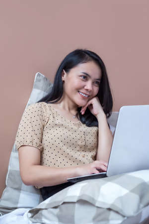 Asian woman relaxing on bed with laptopの写真素材