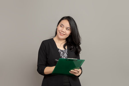 Beautiful woman is imagining while holding a pen and clipboardの写真素材
