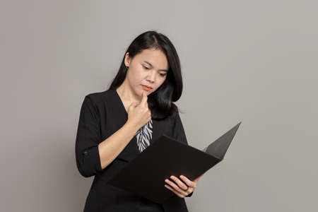 Business woman is imagining with pen on cheek while holding clipboardの写真素材