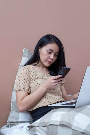 Woman with laptop on bed with flat face expressionの写真素材