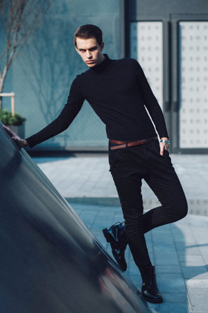 Man model in strict black dress in a modern architectural environment.It rests on the metal wall. Fashion styleの写真素材