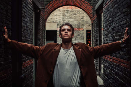 Man in coat rests his hands on the wall and looking up near the brickwall. Fashion style.の写真素材