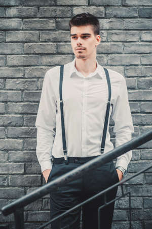 Young stylish man model in classic clothes posing near the brick wall. Fashion shotsの写真素材
