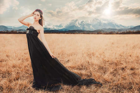 Beautiful girl in a black dress with flowers in the mountains in the background. Fashion shotの写真素材
