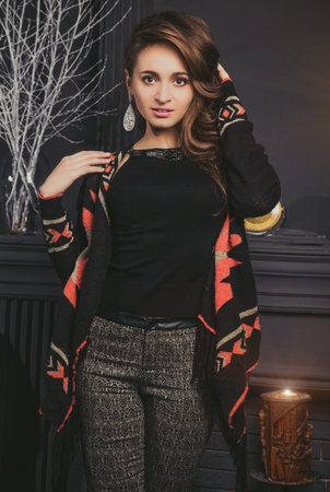 Beautiful brunette girl in fashion clothes sitting posing on the old vintage chear near fireplace....