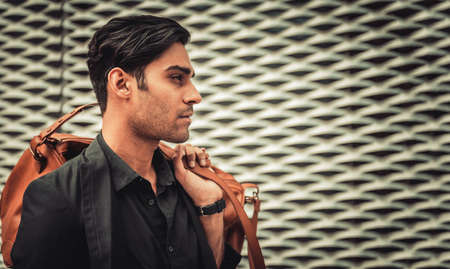 Stylish model looking man profile with handbag on his shoulder in modern architectural environmentの写真素材