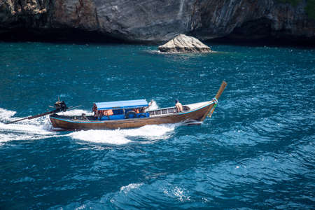 Wooden boat sailing on blue sea against rocks mountains.の写真素材