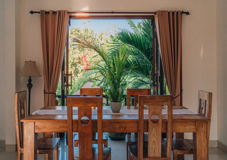 Wooden table with chairs at window with nature view. Potted tropical plant on table, summer balinese villaの写真素材