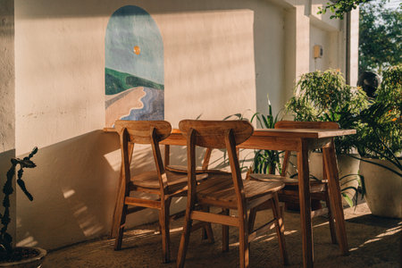 Wooden table with chairs at white wall with decorative painting. Outdoor summer table in tropical gardenの写真素材