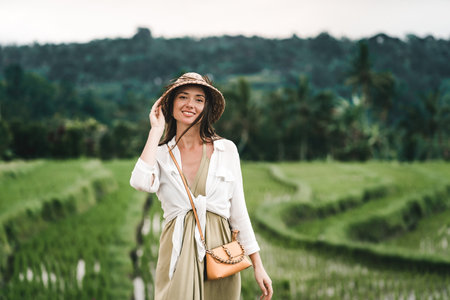 Close up shot of beautiful girl with traditional balinese hat on rice terrace background. Smiling lady in paddy fieldの写真素材