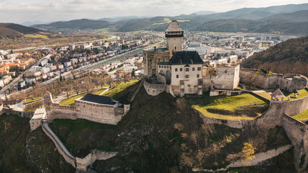 Aerial panoramic view of medieval Trenciansky hrad and Trencin town in Slovakia. Overhead high angle scene of old buildings, stone walls and towers of romantic castle, historic museum on rocksの写真素材