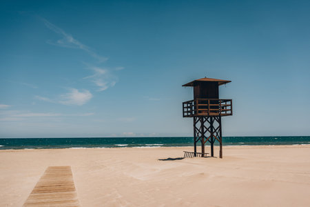 A solitary lifeguard tower standing on an empty, sandy beach with the sea and sky in the background. Sant Antoni beach, Cullera, Spainの写真素材