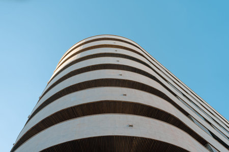 Low-angle view of a modern curved building with horizontal lines. The sleek design and architectural...