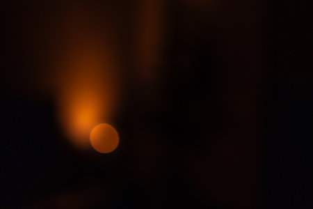 Abstract defocused warm light source in a dark room, creating a moody and atmospheric effect. The soft orange glow contrasts with the deep shadows, suggesting a calm and serene ambiance.の写真素材