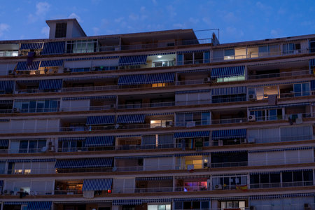 A residential building in Alicante, Spain with striped awnings and illuminated balconies at dusk, blending natural light and urban living.の写真素材
