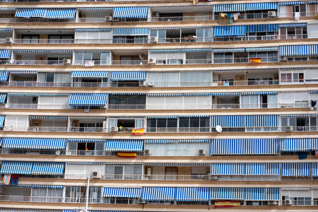 A residential building in Alicante, Spain, brightly lit by the sun, with blue striped awnings covering the balconies on a clear day.の写真素材