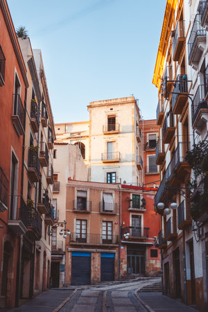 Venture into this charming alleyway adorned with vibrant buildings that warmly bask in the sunlight beams in Tarragona, Spainの写真素材