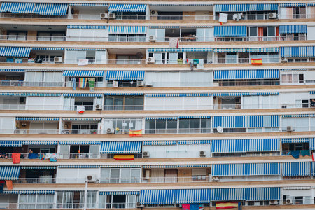 A multi-story residential building in Alicante, Spain featuring blue and white striped awnings over balconies, creating a repetitive pattern.の写真素材