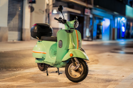 A charming green scooter is parked casually on a bustling city street, illuminated beautifully by ambient night lightsの写真素材