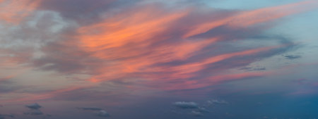 A panoramic view of a sky during sunset with vibrant clouds spread across the horizon, giving a...