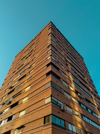 Upward view of a tall brick apartment building with geometric lines, air conditioners, and windows,...