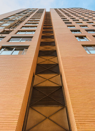 Upward view of a contemporary high-rise building featuring a geometric brick facade, symmetrical...