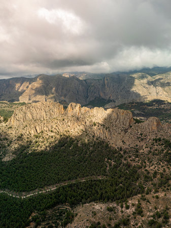 Aerial landscape of Puig Campana region in Spain, featuring rugged mountain peaks, dense green forests, and dramatic cloud shadows, ideal for nature, travel, and adventure themes.の写真素材