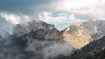 Stunning view of rugged mountains and dramatic clouds in the Puig Campana region, Spain. Perfect for nature, travel, adventure, and scenic landscape backgrounds.の写真素材