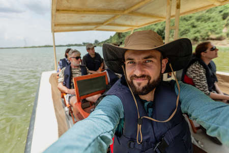A young man in a hat takes a selfie of the boat with tourists. on March 14, 2018 in Queen Elizabeth National Park, Ugandaのeditorial素材