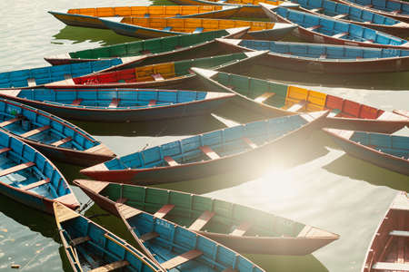 Multicoloured wooden boats under rays of sunlight on Phewa lake in Pokhara, Nepalの写真素材